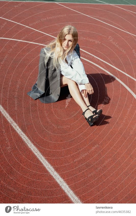 Young blonde female wearing heels and jacket, sitting on a backetball sport field girl attractive lifestyle adult person calm outdoors pretty young stress-free