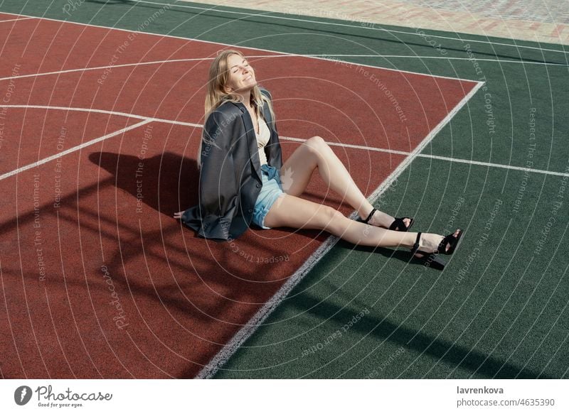 Young blonde woman in high heels and jacket sitting on backetball court Woman single adults on one's own Attractive pretty Smiling Happy Blonde Calm Cute Girl