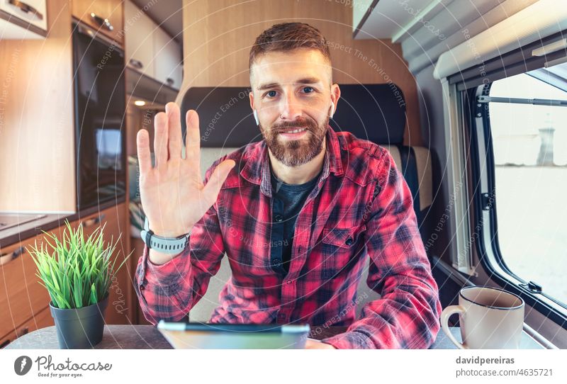 Man waving on video call from his campervan man looking camera videoconference remote work camper van smiling wireless earphones person business chat interview