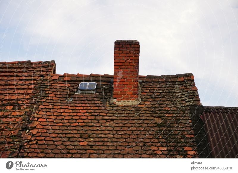 old tiled roof of a row house with an unplastered chimney, a small skylight and adjacent corrugated metal roof / live Roof Tiled roof Skylight Old Red