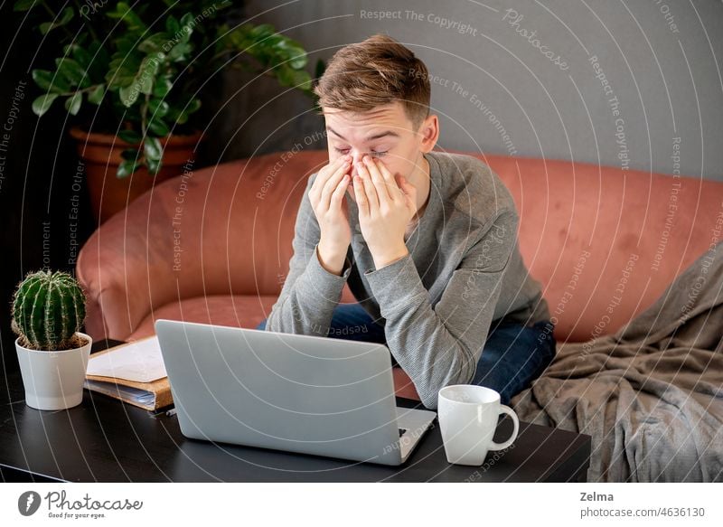 Feeling tired. Frustrated young  man looking exhausted and covering his face with hands while sitting at laptop his home working place headache pain student