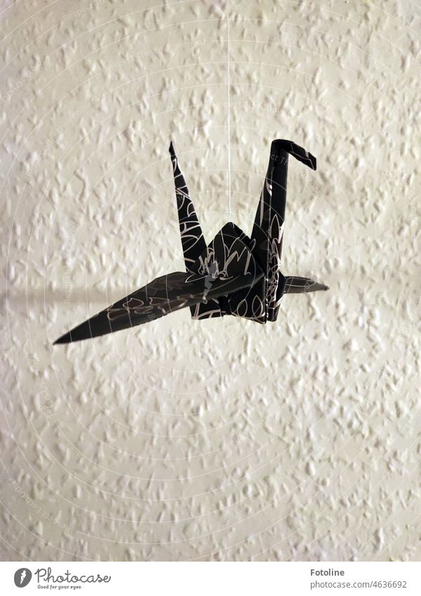 An origami crane hangs on a silk thread in front of a wall with woodchip wallpaper Origami Ingrain wallpaper Crane Origami Paper Interior shot