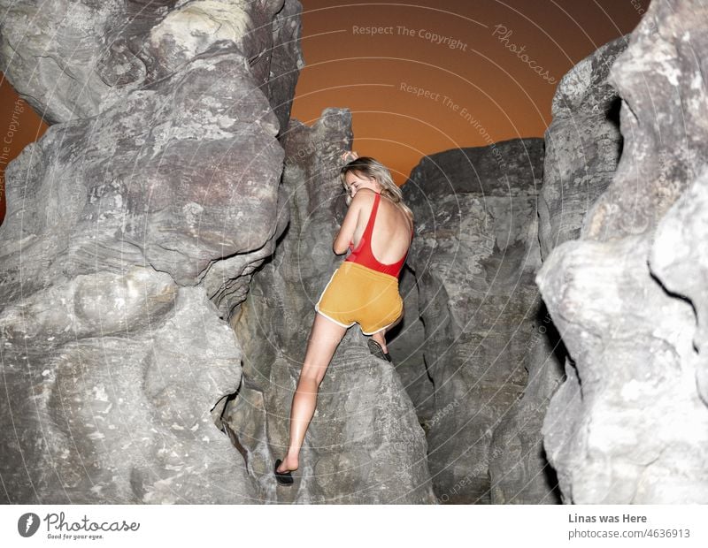 Some rocks to climb in Vietnam for this gorgeous blonde girl. Dressed in a red swimsuit, orange shorts, and slippers she is not so ready for climbing. A beautiful sunset scenery accompanies her.