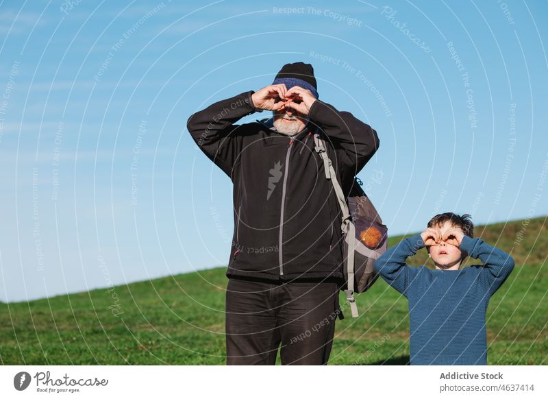 Grandfather and grandson making binocular gesture in nature grandfather observe curious watch discovery explore boy man spy environment interest grass grassy