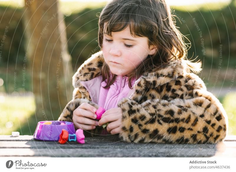 Girl playing with toys at table in park curious girl interest child spend time adorable outerwear innocent carefree kid entertain childhood casual development