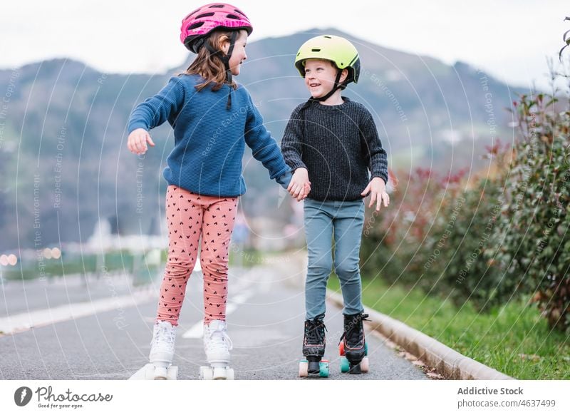 Kids holding hands riding on roller skates on road children ride hobby childhood leisure spend time nature activity sibling practice kid girl sister brother boy