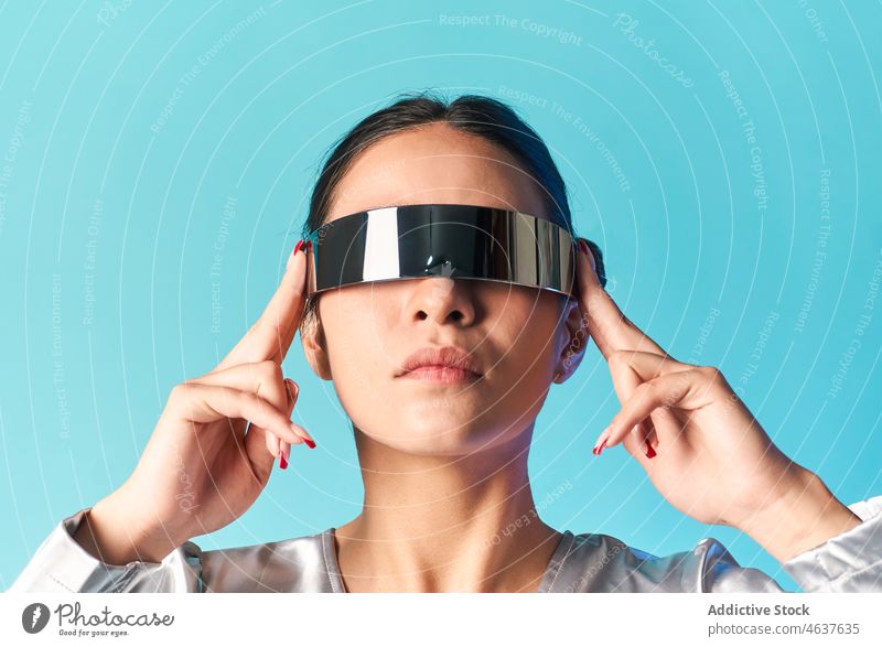 Confident young ethnic lady using mirrored VR glasses in blue studio woman virtual reality experience style futuristic vr augmented portrait entertain digital