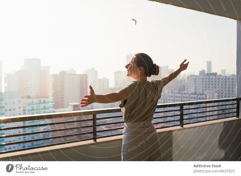 Content young woman enjoying sunny day standing on balcony with outstretched arms smile cityscape vacation terrace tourist delight eyes closed happy tourism