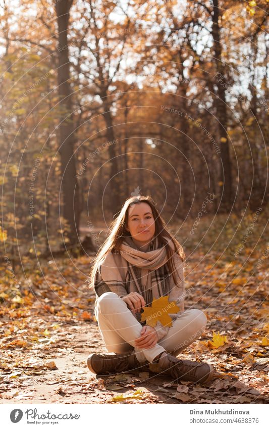 Young woman with beige scarf and jeans walking in autumn park at sunset with warm sunshine. Relaxing moments in nature, millennial girl being happy and smiling.