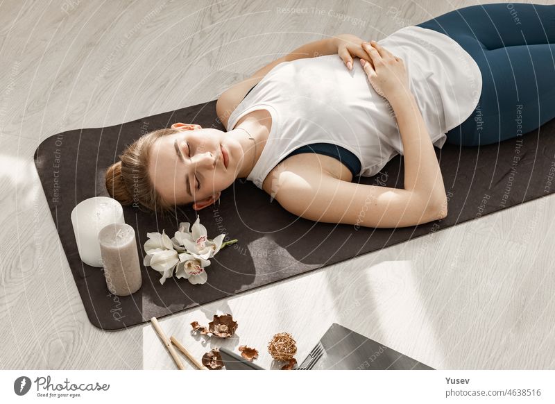 Young beautiful sporty blonde girl is engaged in hatha yoga in a modern light studio. She lies on the floor and meditates with her eyes closed. Close-up young