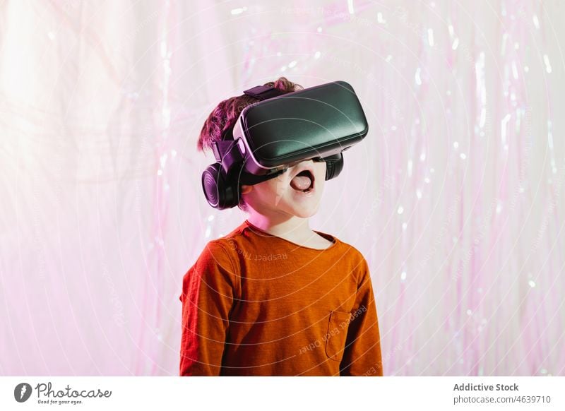 Amazed boy in VR glasses in studio kid vr shock amazed goggles virtual reality cyberspace child headset entertain neon light astonish device innovation