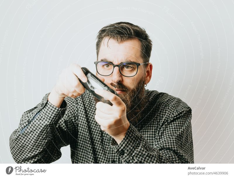 Young handsome bearded man with glasses playing with a video game controller expresful concentrations faces funny over isolated white background. Gaming medium age concept. Copy space concept