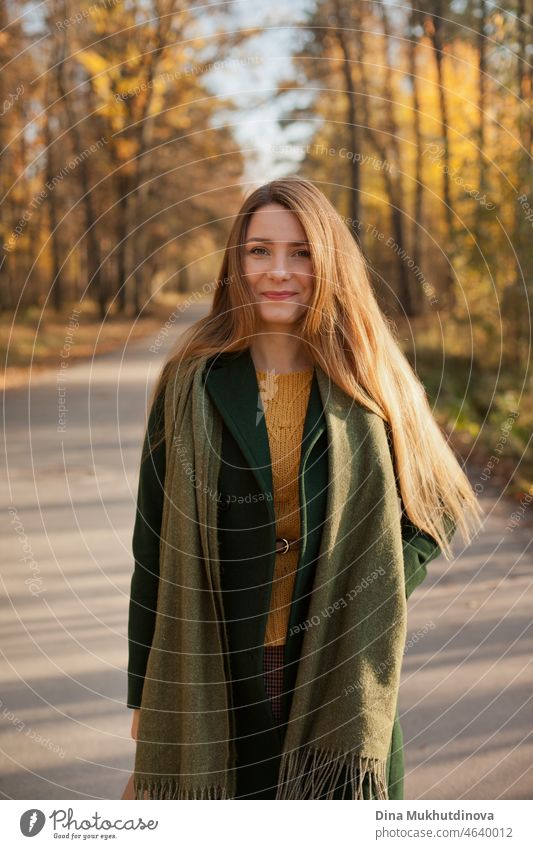 Beautiful woman in green coat and yellow sweater in autumn park near trees with yellow leaves at sunset. Spending time in nature to keep peace in mind, relaxing moments and minfullness. Autumn style and fashion, casual clothing.