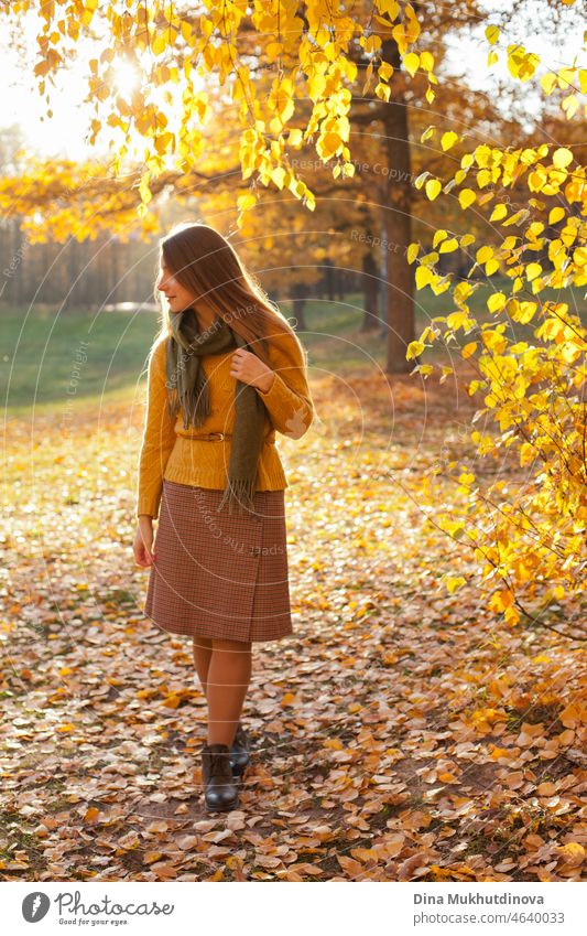 Beautiful woman in yellow sweater in autumn park near trees with yellow leaves at sunset. Spending time in nature to keep peace in mind, relaxing moments and minfullness.  Autumn style and fashion, casual clothing.