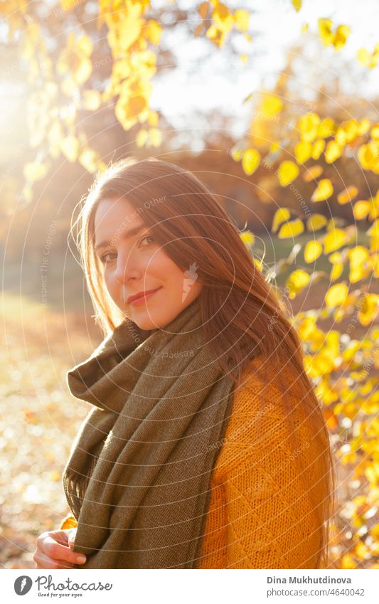 Beautiful woman in yellow sweater and green scarf  in autumn park near trees with yellow leaves at sunset. Spending time in nature to keep peace in mind, relaxing moments and minfullness.  Autumn style and fashion, casual clothing.