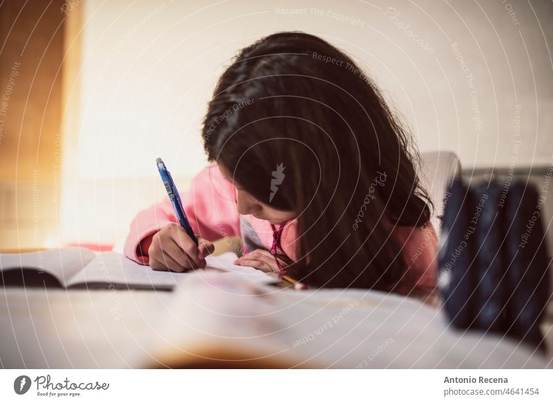 A girl does her homework at home writing concentrated children chores domestic realistic tracksuit books student activity people caucasian spanish lifestyle