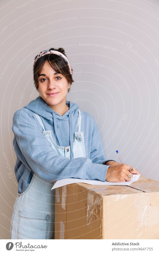 Young woman signing rent contract during relocation relocate box smile paper new real estate belonging female young happy brunette casual glad cardboard stack
