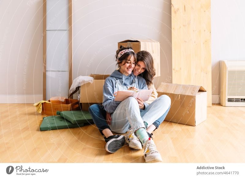 Cheerful lesbian couple writing in diary during relocation write relocate smile hug belonging box together notebook new women cardboard mortgage happy move in
