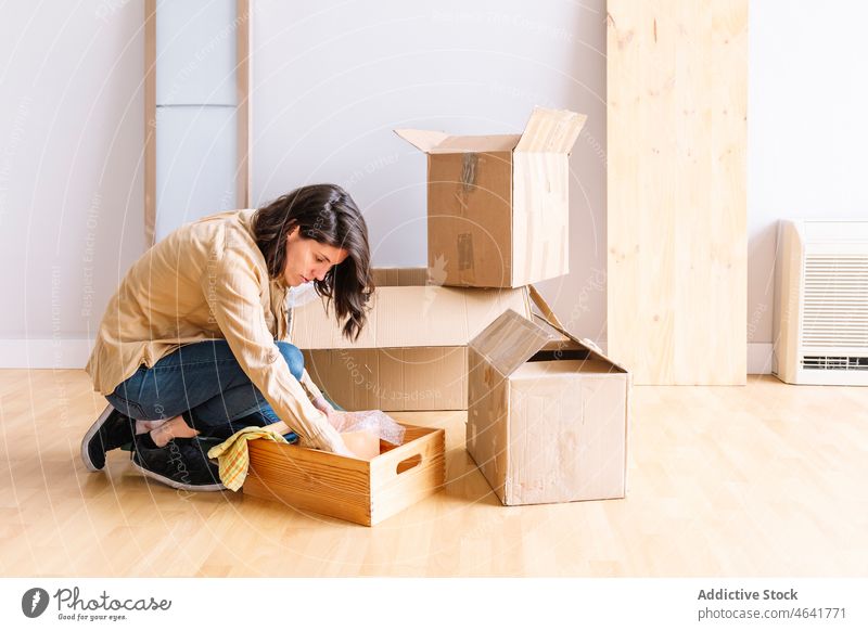 Female homeowner unpacking belongings on floor woman box relocate room new female move in property stuff kneel wooden light apartment casual package
