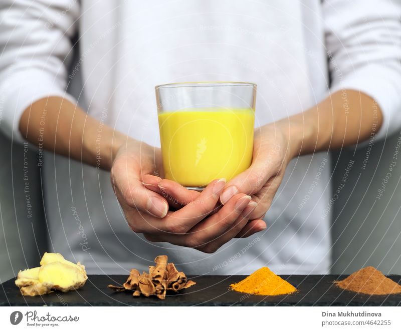 Hands holding a glass of golden turmeric milk - alternative herbal medicine concept and naturopathy drink latte spice yellow detox health powder remedy