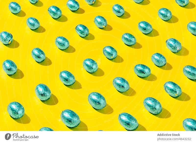 Pattern of green foil chocolate eggs on a yellow background. group shiny sphere three-dimensional abstract ball concept design pattern texture copy space easter