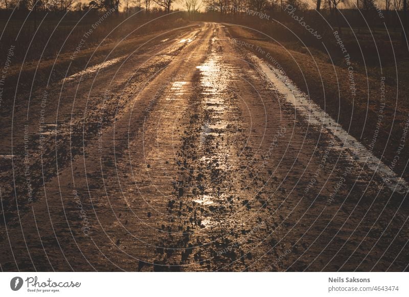 dirty sand and gravel road with puddles in sunset golden light abstract background blue brown clay close-up cloud country countryside day diagonal drive earth
