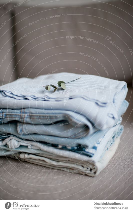 A stack of clothes in light blue color palette  folded neatly on a sofa or couch. Spring organizing and decluttering at home. Apartment living and cleaning. Organizing clothes neat and clean.