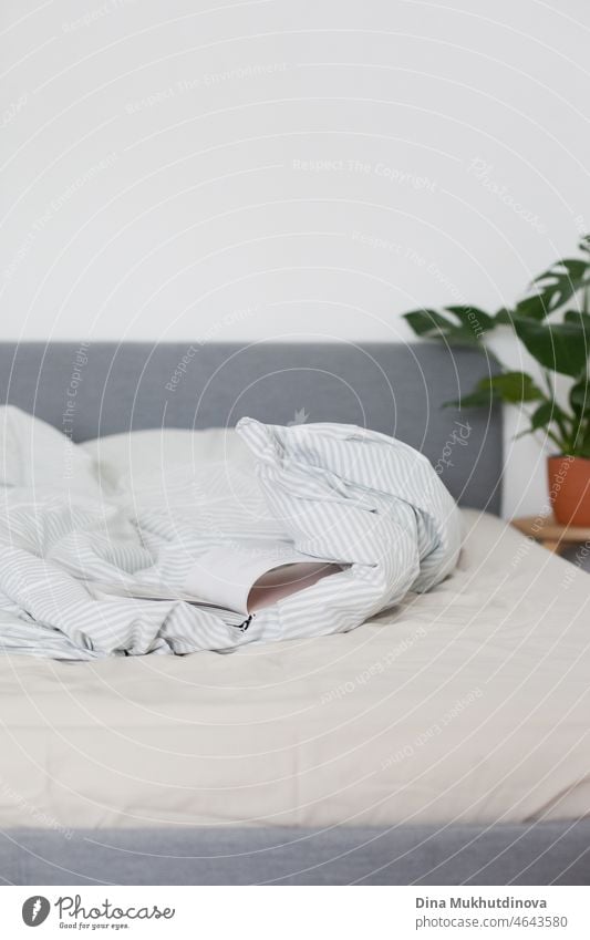 an open book lying on the bed in cozy apartment home in minimalist scandinavian style in neutral light colors with a green plant indoor bedroom blanket comfort