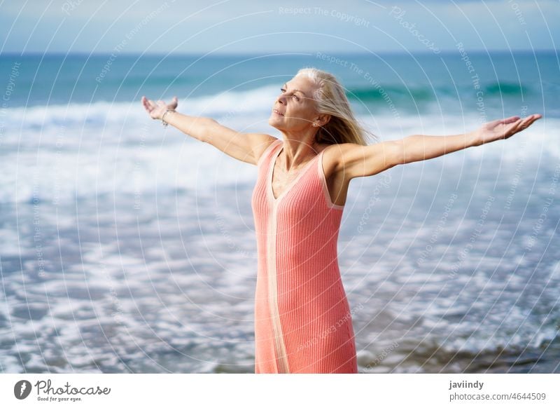 Beautiful mature woman opening her arms on a beautiful beach, enjoying her free time senior old person retirement female lifestyle happy sea holiday relaxing