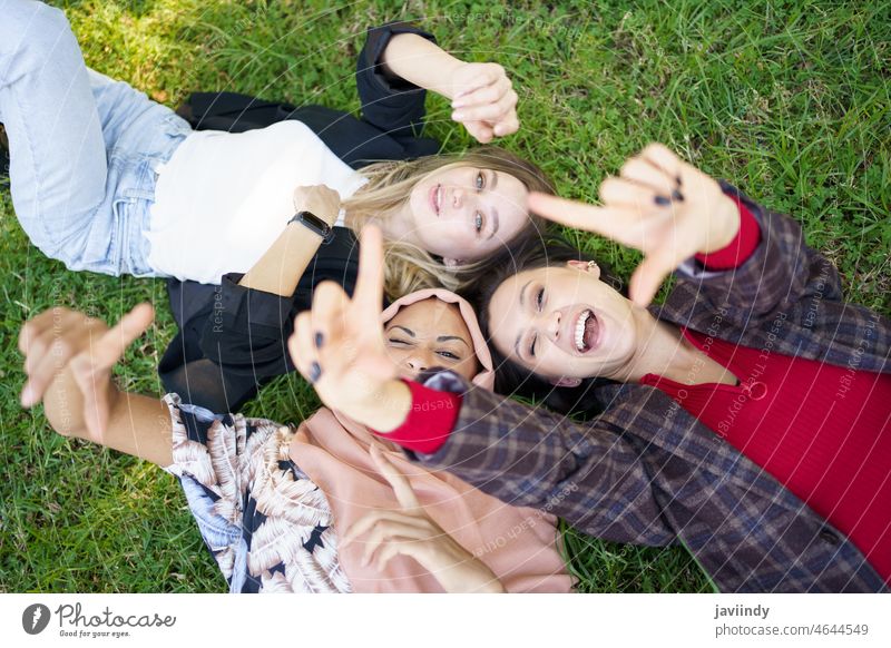 Cheerful ladies gesturing camera while lying on grass women lawn laugh spend time friend having fun playful gesture together joy friendship young diverse