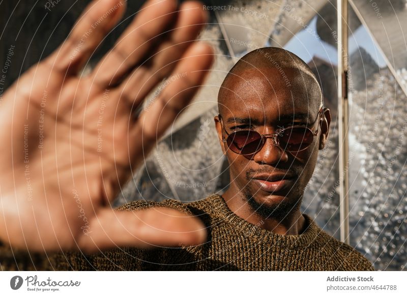 Black man covering from sun with hand sunlight sunny street building appearance style palm sunglasses serious male bald confident trendy african american black