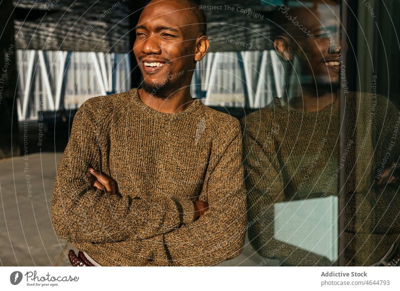 Cheerful black man near glass building glass wall reflection street urban appearance style fashionable city male laugh arms crossed bald african american
