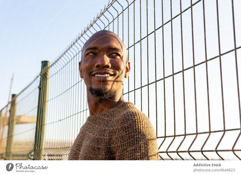 Cheerful black man near fence street barrier sunshine happy urban pastime appearance style city male bald african american unshaven guy self assured smile beard