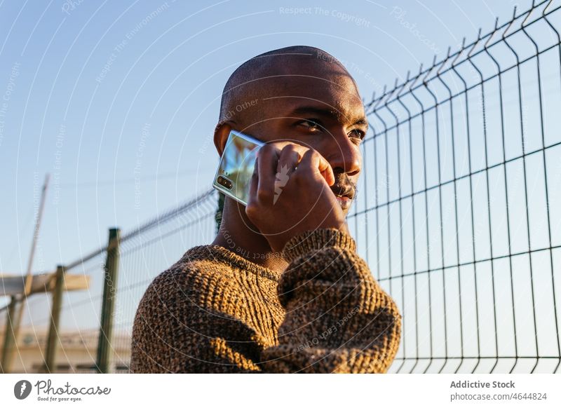 Black man talking on smartphone near fence phone call conversation discuss street connection communicate city barrier metal fencing style building appearance