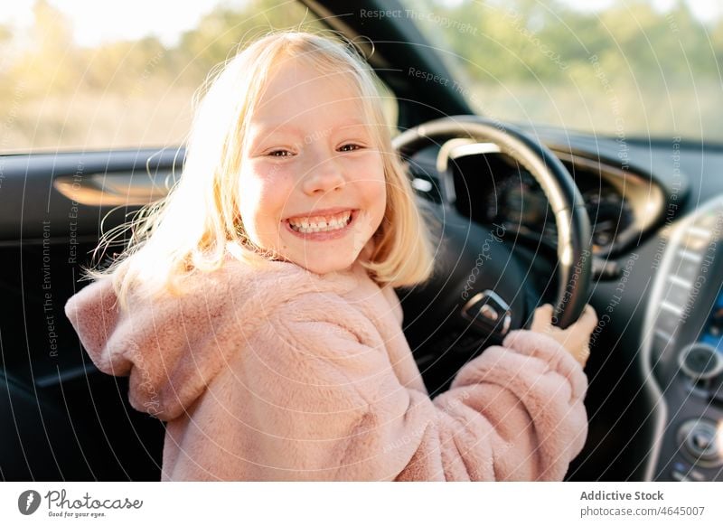 Happy girl sitting on driver seat kid car automobile steering wheel ride trip commute having fun playful modern happy vehicle positive cheerful smile journey