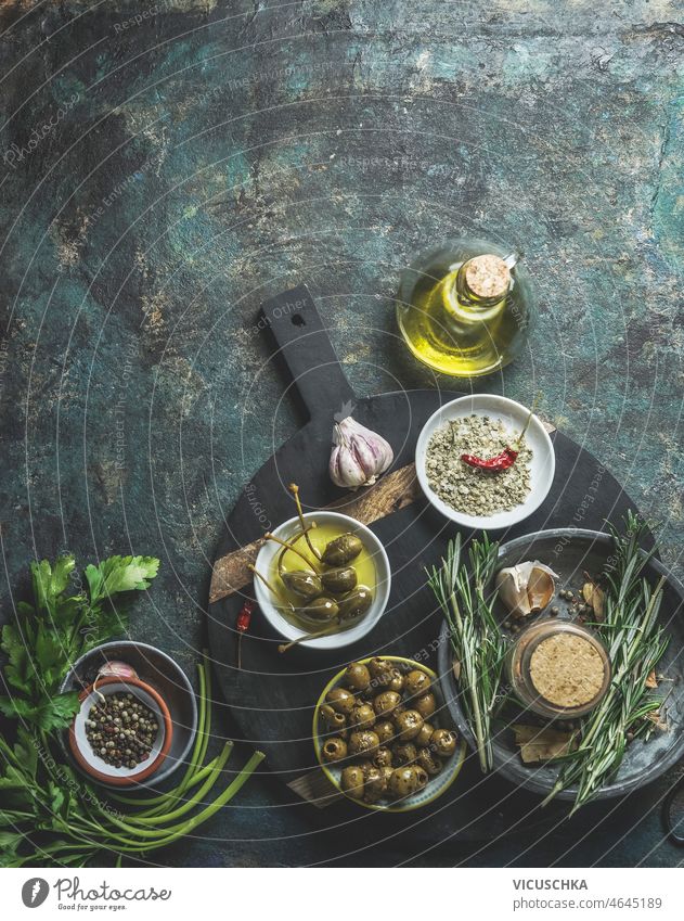 Food background with olives, olive oil, capers, salt, garlic and rosemary on rustic kitchen table food background mediterranean food cooking top view above dark