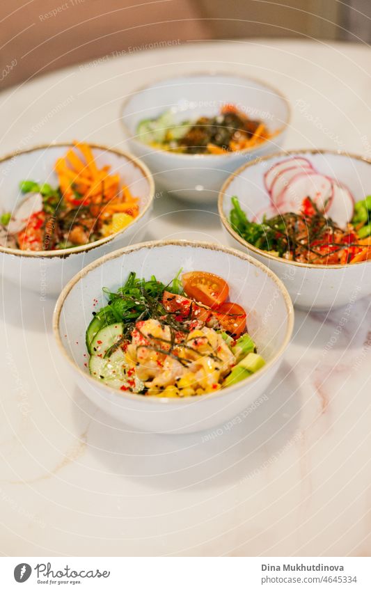 Healthy eating - bowls of poke Hawaiian dish with vegetables and seafood, tasting exotic international cuisine meals. Colorful food poke bowls on a white marble table at the restaurant