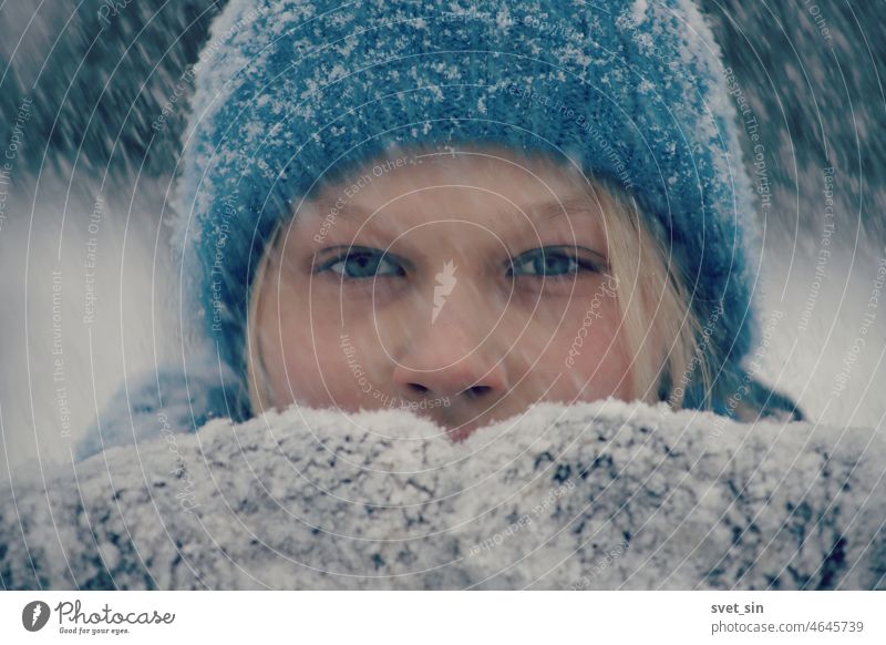 Portrait of a blonde girl in a blue knitted hat and snowy mittens in a heavy snowfall. It's snowing. portrait outdoors Winter Snowfall white face pretty hair