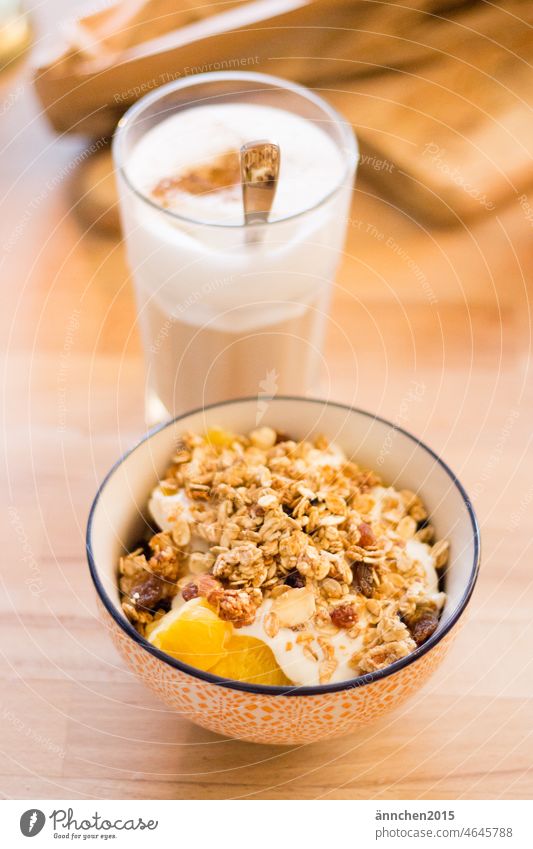 in the front of the picture is a cereal bowl with fruit, granola and cottage cheese behind it is a latte macchiato in a glass Coffee Breakfast Eating Cereal