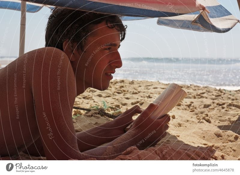 Beach life: Teenager looking at the sea while reading younger Ocean Reading Book Boy (child) teenager Sunshade Reading matter Novel vacation relaxed Sand