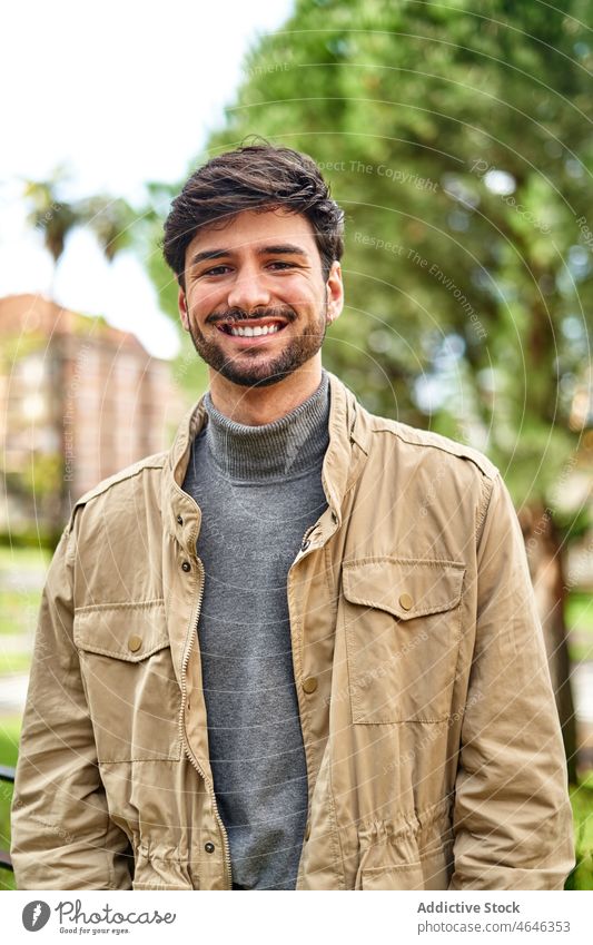 Smiling bearded man in jacket standing in park positive portrait personality cool individuality appearance glance happy male content glad smile optimist