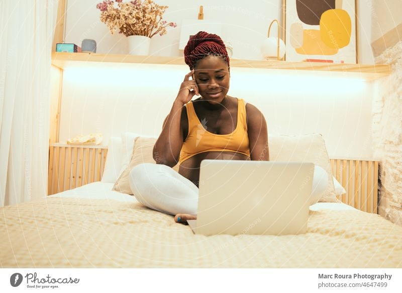 pregnant black woman relaxing on bed with a laptop at home african apartment bedroom belly business care comfort computer cool couch elegant excited female girl