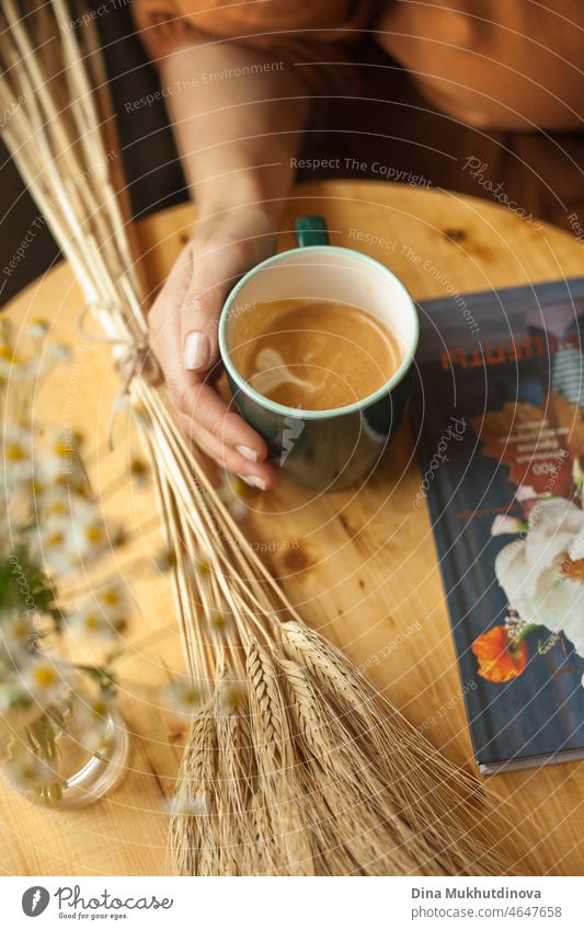 Drinking coffee from a green mug at cafe, on a wooden table with a book and wheat bouquet drinking pretty female portrait relaxation young adult holding indoors