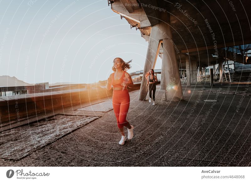 Two young girls jogging during a sunset, backlighting, train on ruban ambient concept. Working out clothes, top and leggings, African woman fitness. Sunset ambient, slim bodies.