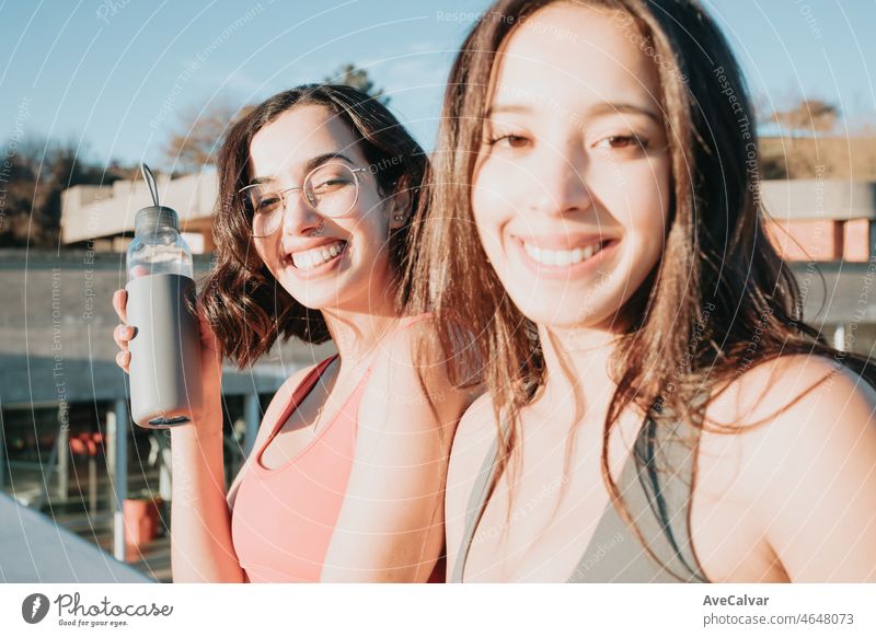 Portrait of two young sporty girls smiling to camera while resting after jogging. Working out clothes, top and leggings, African woman fitness. Sunset ambient, slim bodies.