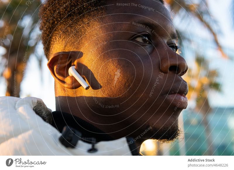 Black meloman with earbuds in nature using earphones true wireless tws park music listen sound male black audio african american casual entertain melody ethnic
