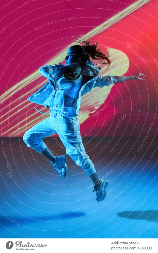 Woman dancing with raised hands in colorful studio woman dancer move skill rehearsal stretch jump happy projector perform female energy dynamic practice