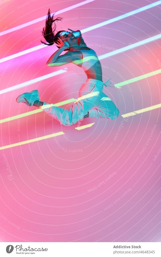 Energetic woman listening to music and jumping in studio headphones happy neon stripe dance active female cool perform hip hop inspiration above ground smile