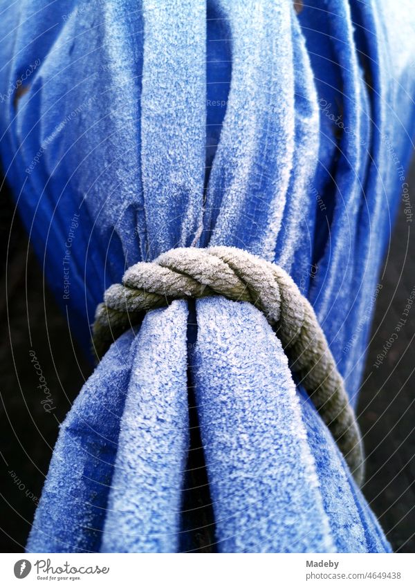Old ship's rope around a blue tarpaulin made of plastic with hoarfrost over a boat trailer in Oerlinghausen near Bielefeld at the Hermannsweg in the Teutoburg Forest in East Westphalia-Lippe