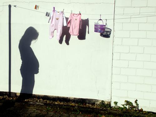 In joyful expectation - On a clothesline hangs freshly washed baby clothes and a basket with clips. The shadow of the expectant mother shows.... it won't be long before the baby comes.